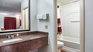 A bathroom with a granite countertop sink, a mirror, a towel rack, and a shower curtain.