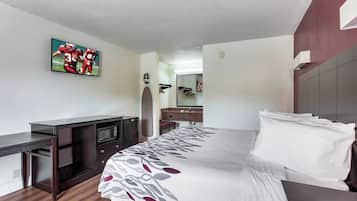 Una habitación de hotel con una cama, un escritorio con televisor, un microondas y un espejo.