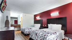 A hotel room with two beds, a wooden floor, a bathroom with a mirror, and a red accent wall. - Red Roof Inn Monteagle - I-24 (Monteagle)