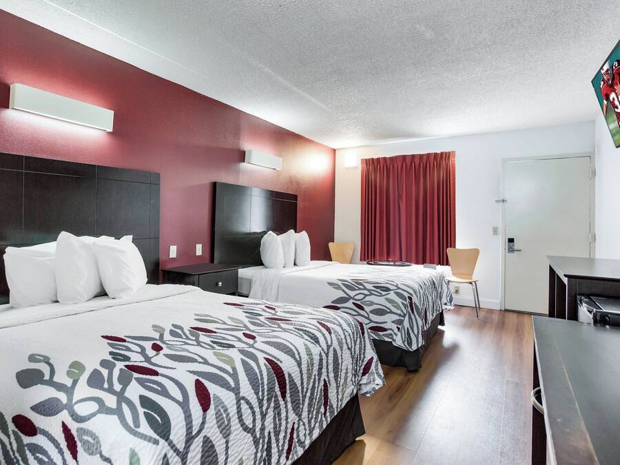 A hotel room with two beds, a TV, a desk, and a door.
