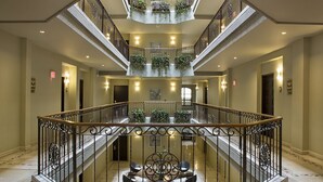 A multi-level atrium with a central staircase, glass railings, and potted plants. - Movich Casa del Alferez (Cali)