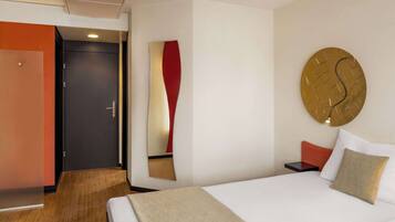 Ein Hotelzimmer mit Bett, Nachttisch, Wanduhr und Tür.