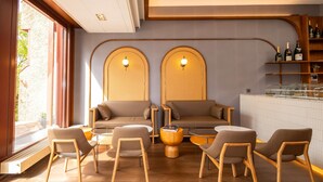 A modern lounge area with a sofa, chairs, and a coffee table. There are arched wall sconces and a bar area with bottles.