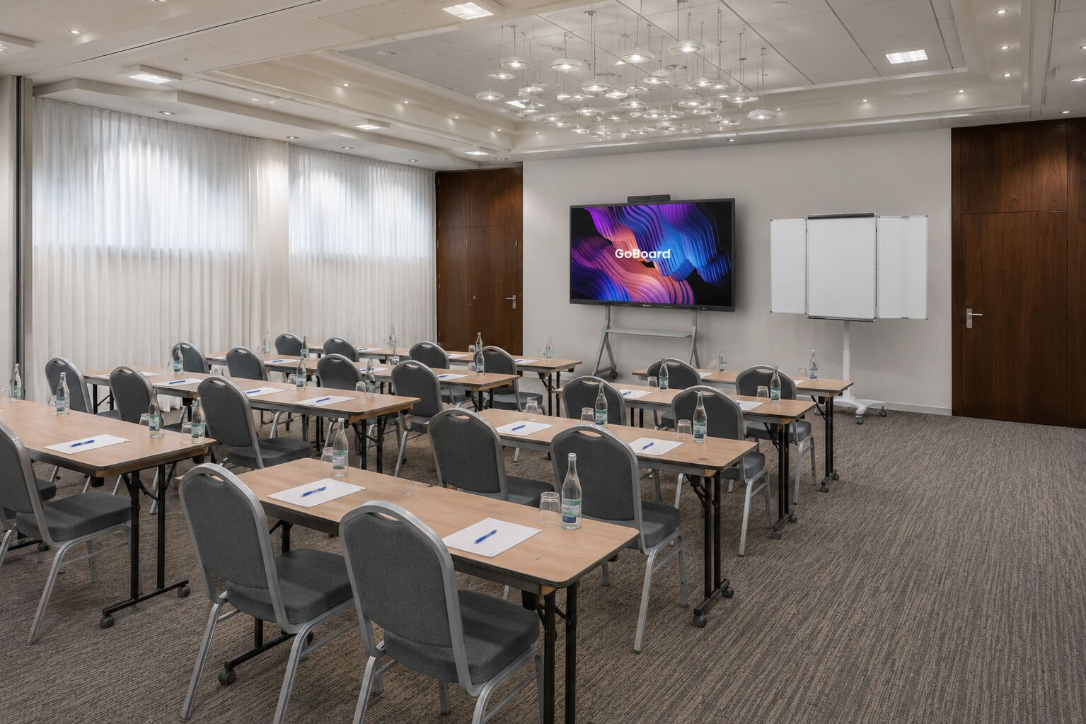Un salón de conferencias con una pantalla grande mostrando 'GoBoard', varias mesas con sillas y una pizarra.