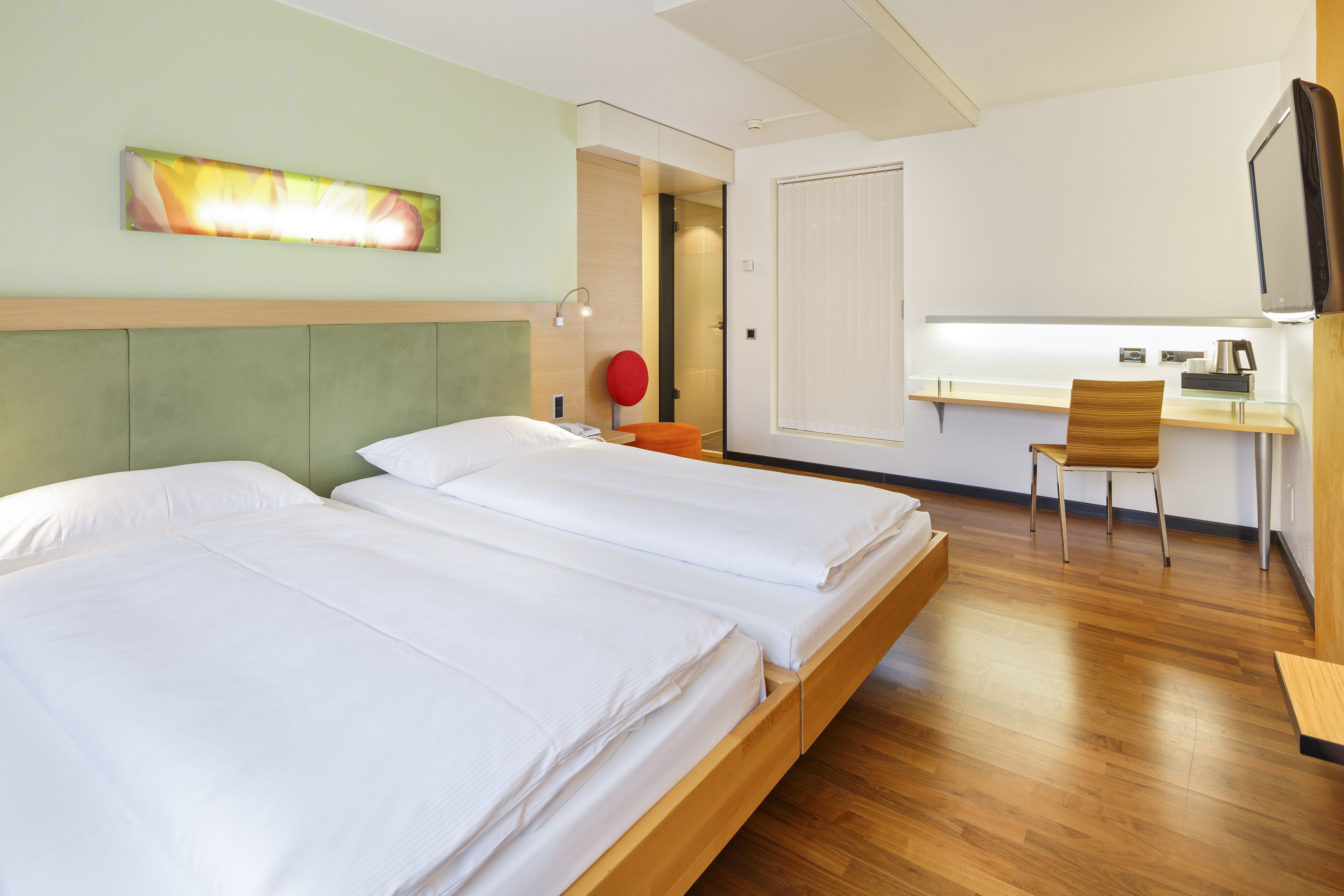 A hotel room with two beds, a desk, a chair, and a TV.