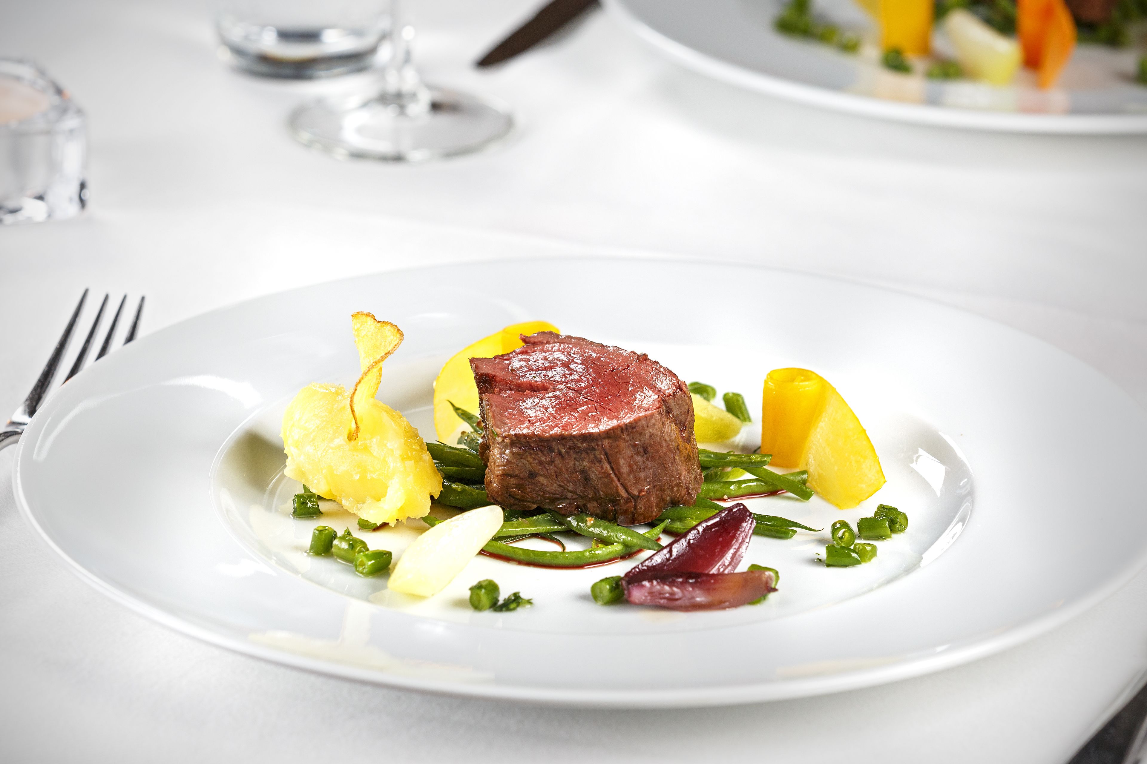 Ein weißer Teller mit einem Steak, grünen Bohnen und gelben Gemüsesorten.
