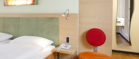 A hotel room with a bed, a nightstand, a red chair, a mirror, and a painting on the wall.