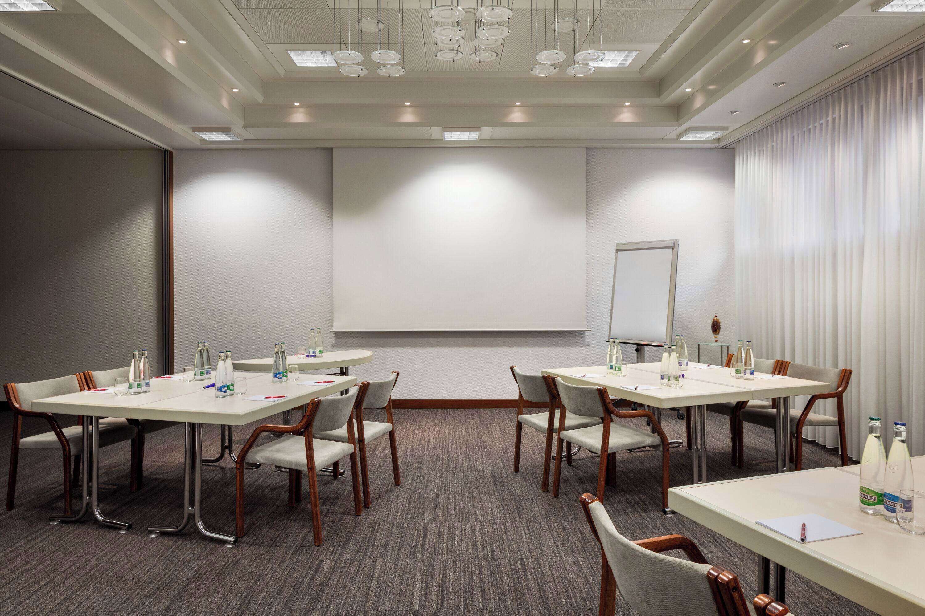 A conference room with four tables, each equipped with chairs, water bottles, and a projector screen.
