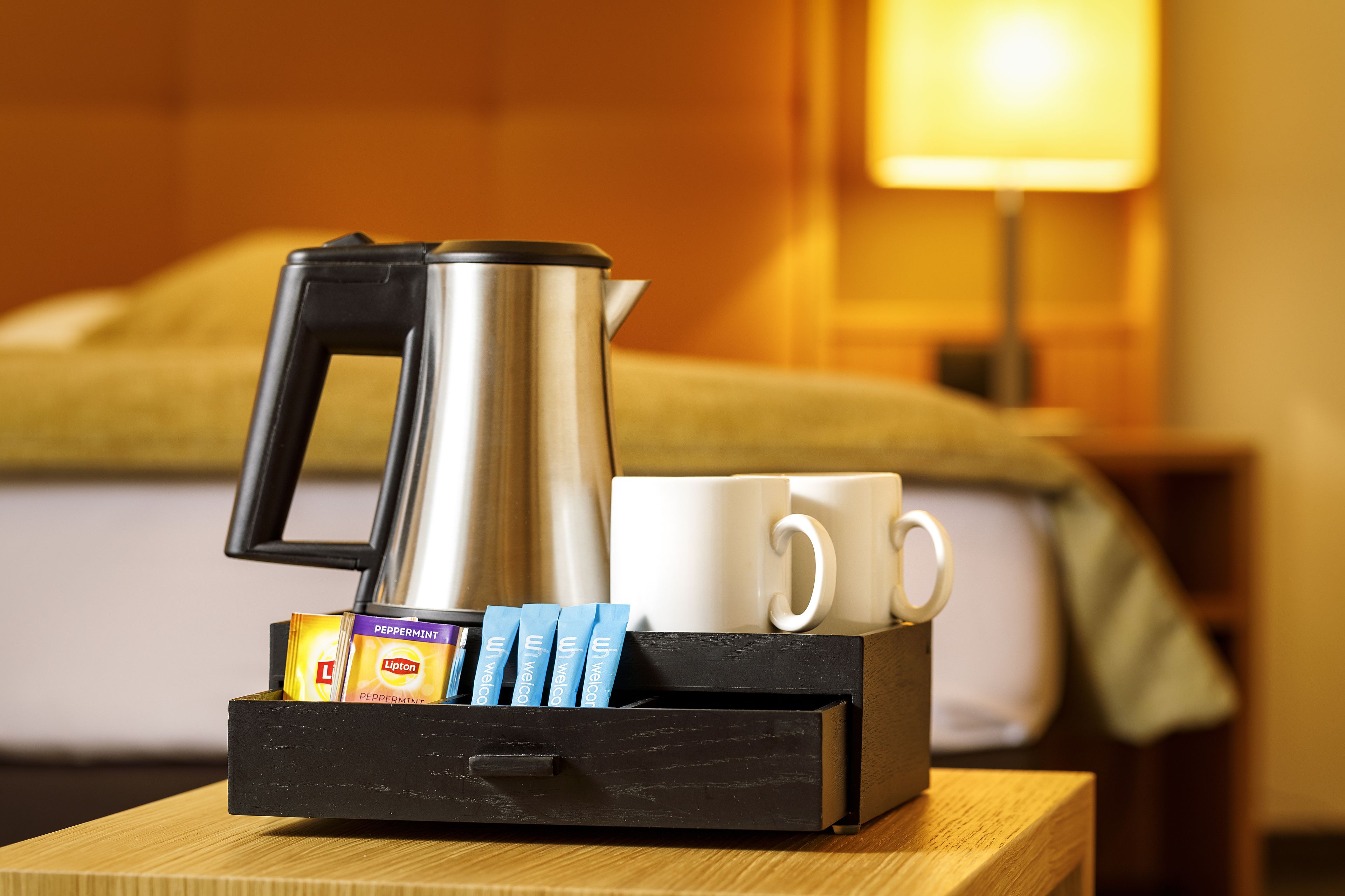 Une machine à café, deux tasses blanches et une boîte de gel douche L'Occitane dans une chambre d'hôtel.