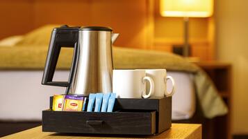 Une machine à café, deux tasses blanches et une boîte de gel douche L'Occitane dans une chambre d'hôtel.