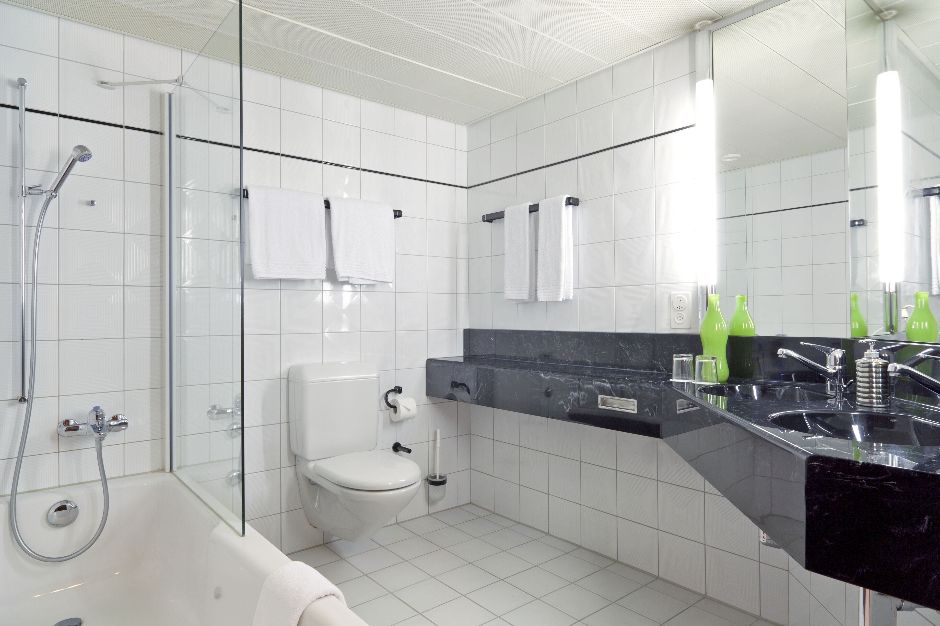 Une salle de bain moderne avec une douche à parois de verre, des toilettes, un lavabo doté d’un plan de travail noir et un miroir qui reflète la pièce.