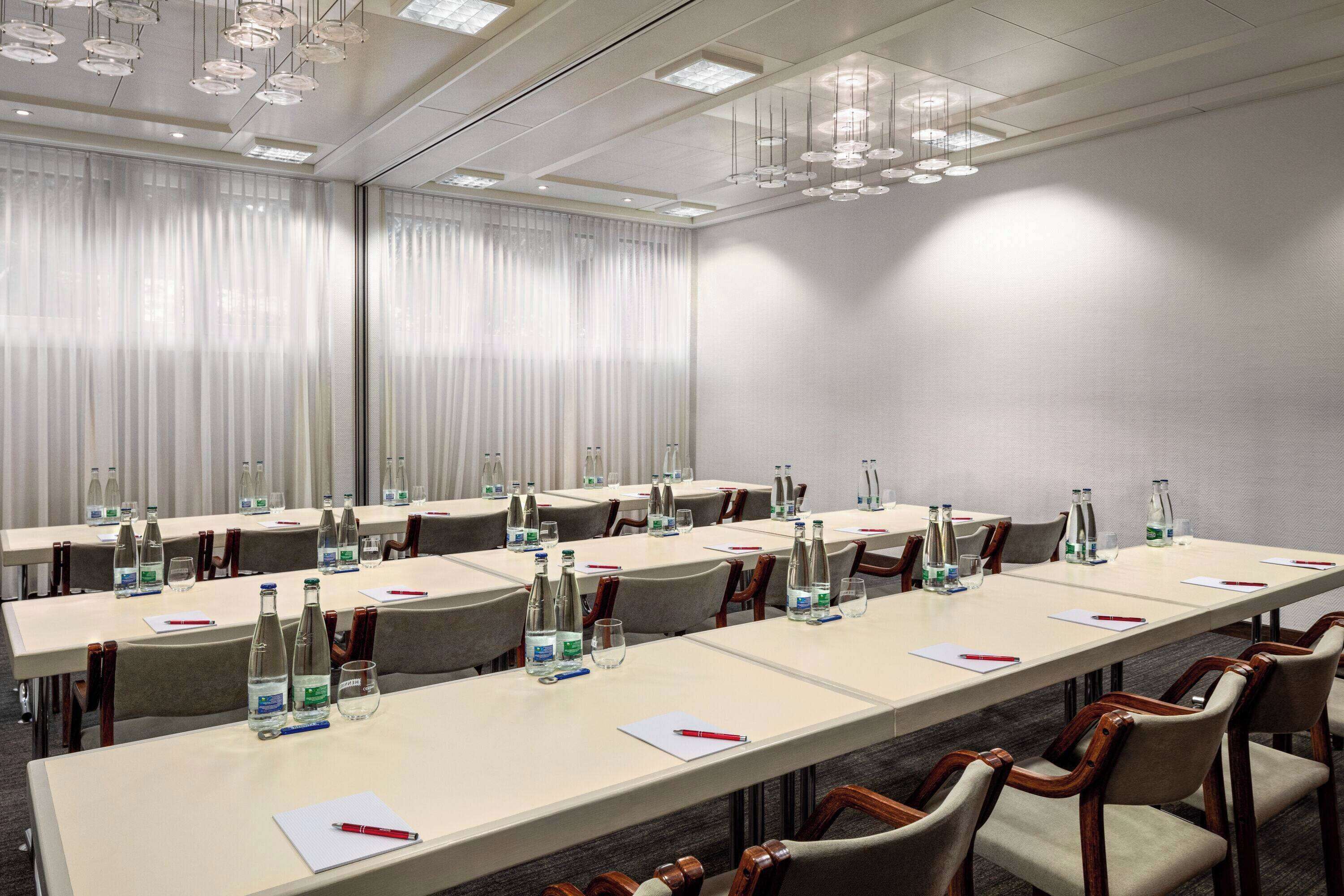 A conference room with long tables, chairs, water bottles, glasses, and pens.