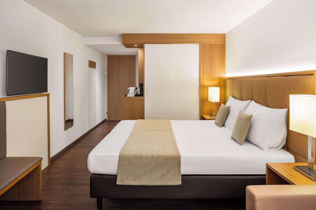 Een hotelkamer met een bed, nachtkastje, lamp en een televisie aan de muur.