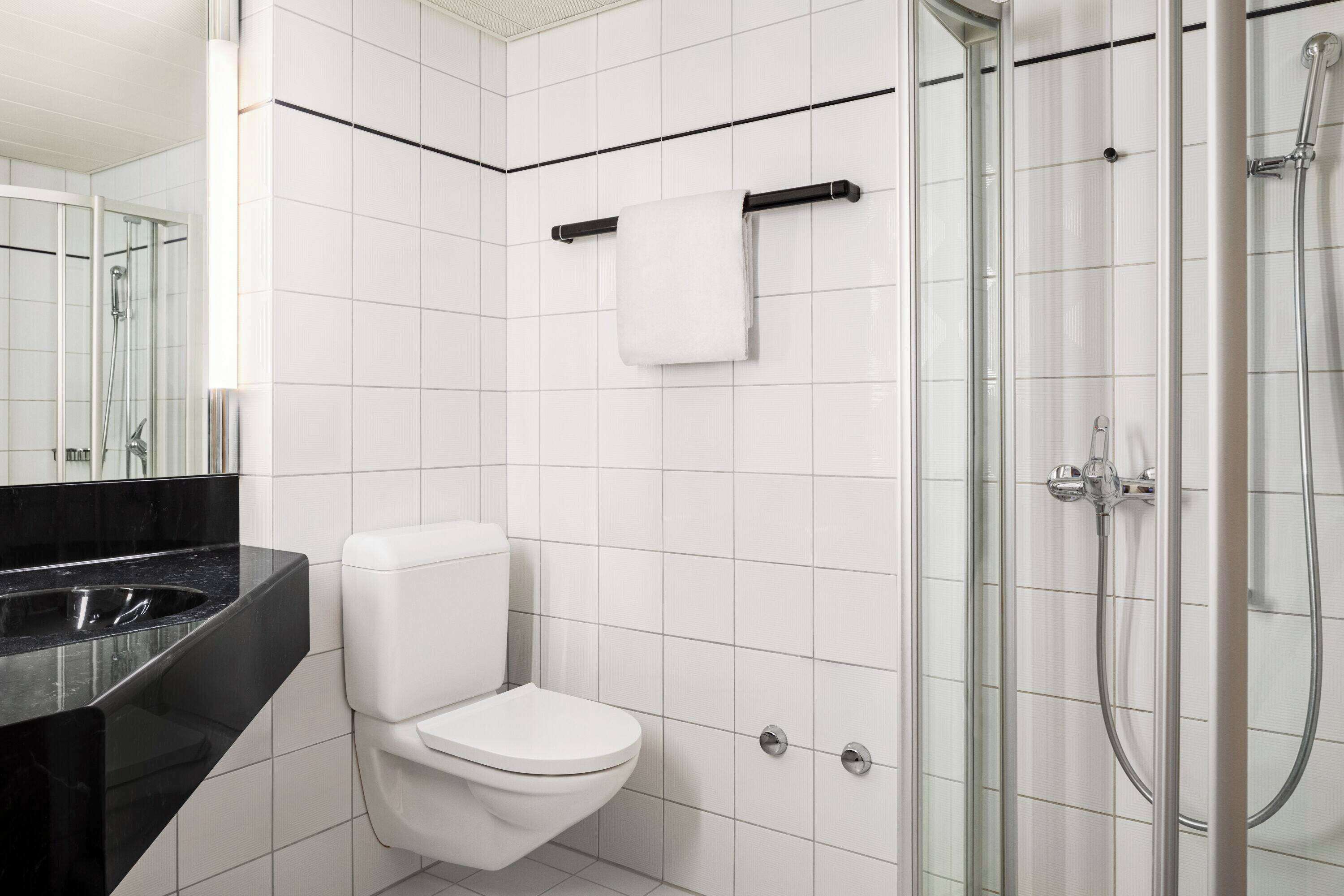 A modern bathroom with a toilet, a glass shower enclosure, and a black countertop.