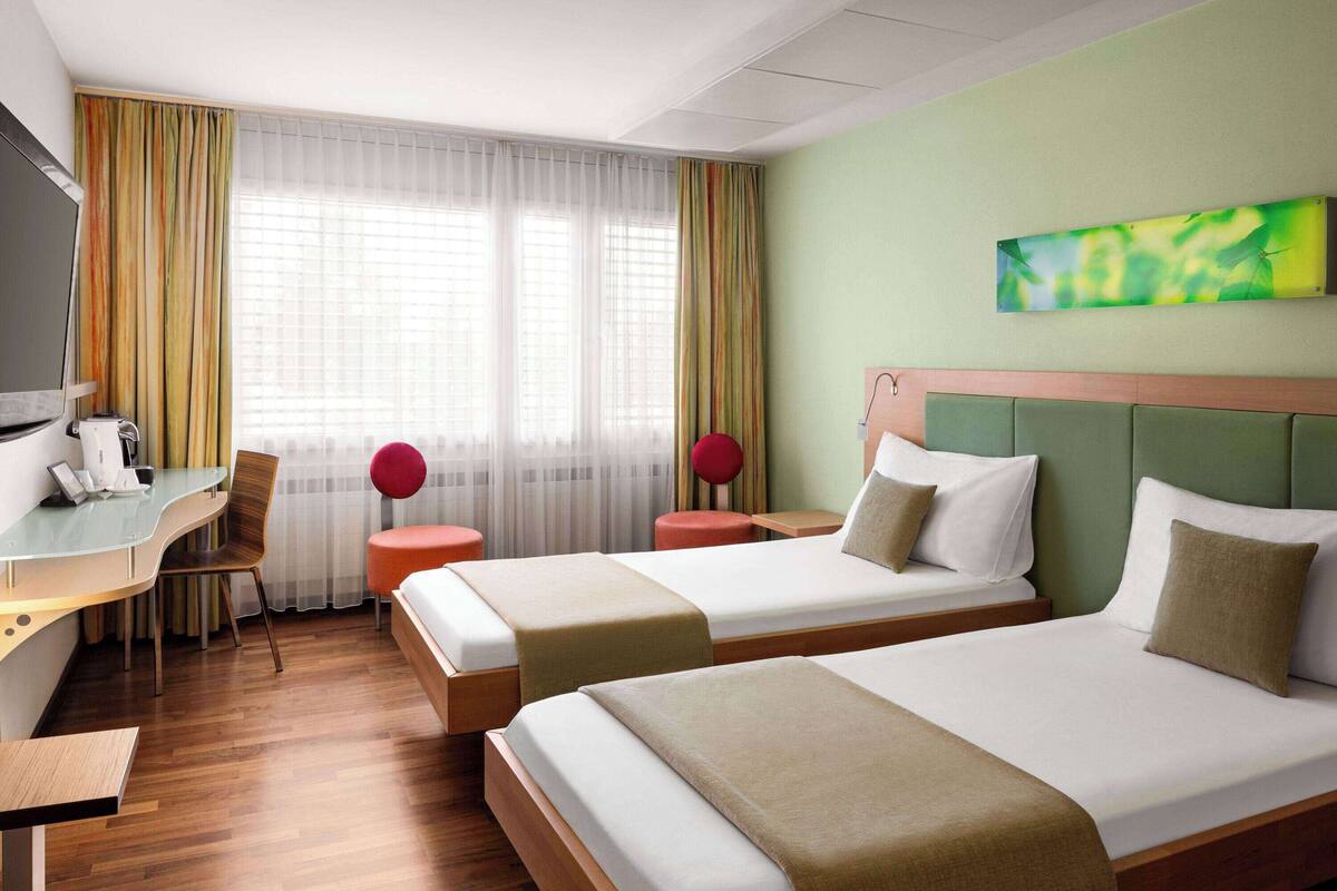 Een hotelkamer met twee bedden, een bureau met stoel, een televisie en een raam met gordijnen.
