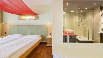 A hotel room with a bed, a shower area, and a large bathtub.