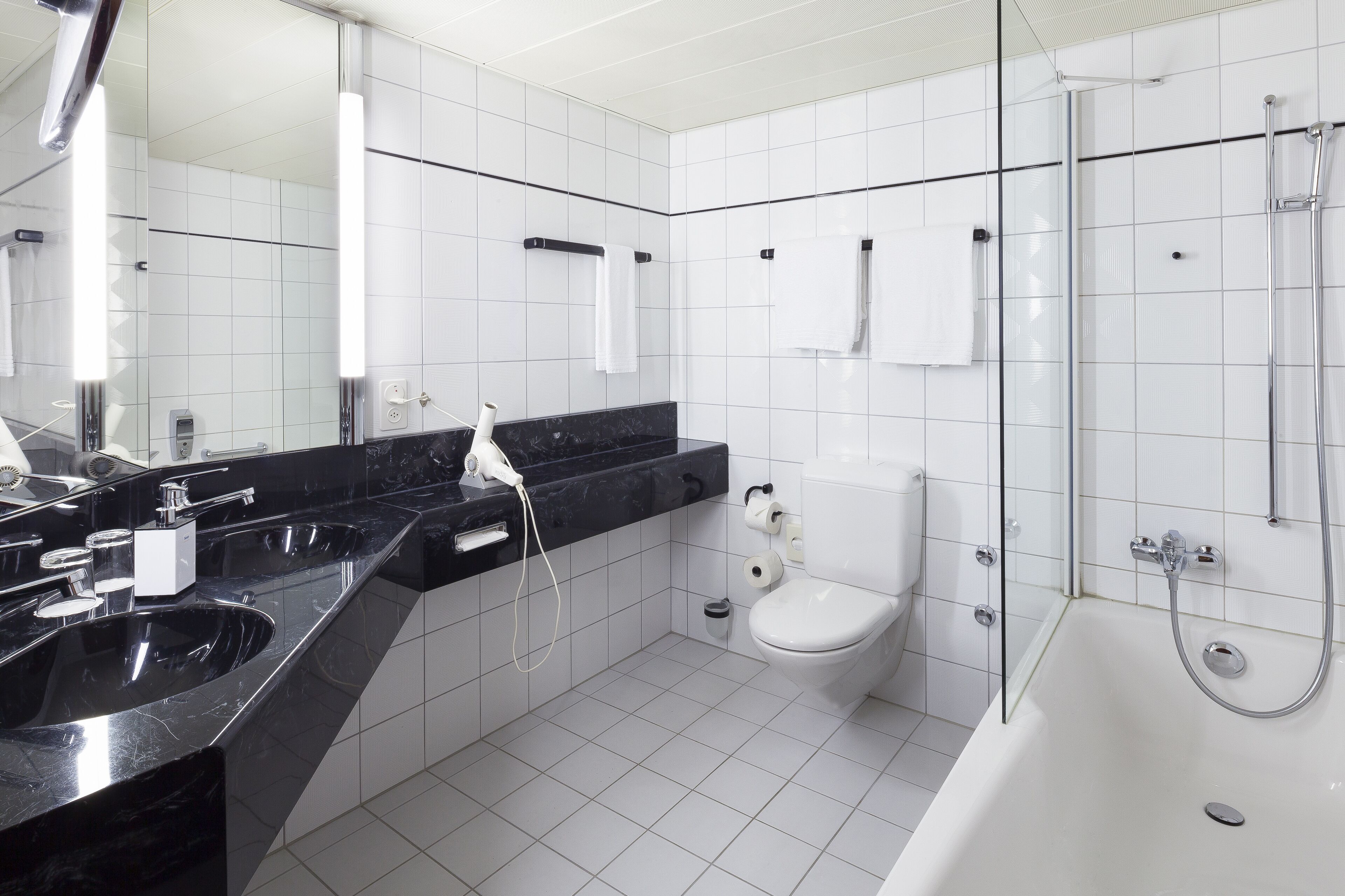 A modern bathroom with a black marble countertop, a white toilet, a glass-enclosed shower, and a large mirror.
