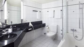 A modern bathroom with a black marble countertop, a white toilet, a glass-enclosed shower, and a large mirror.