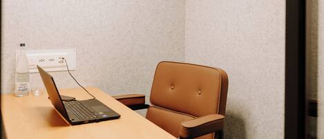 A small, private office with a laptop on a wooden desk, a brown leather chair, and a wall socket.