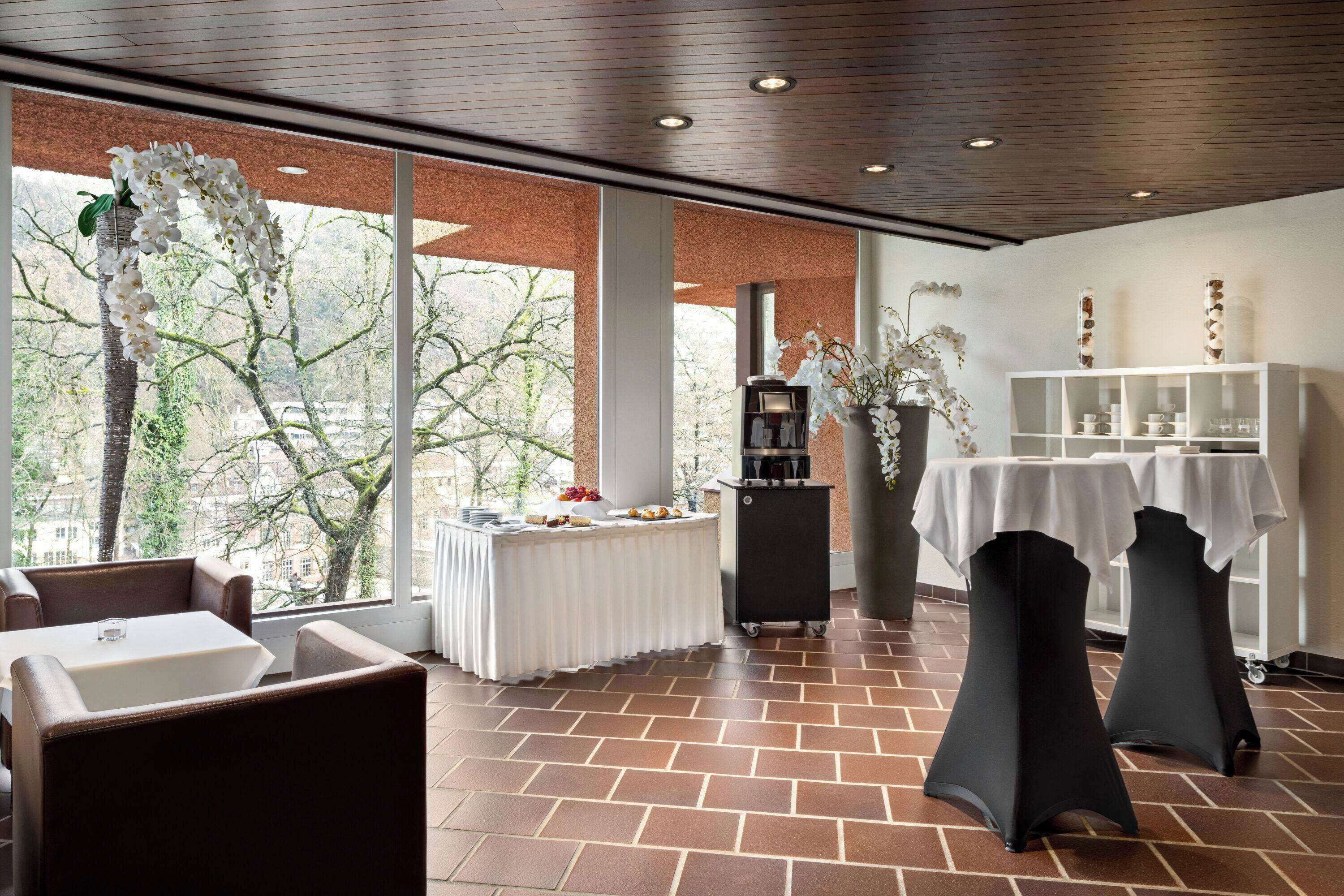 A spacious room with a large window, a buffet table, and two black tables with white tablecloths.