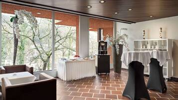 A spacious room with a large window, a buffet table, and two black tables with white tablecloths.