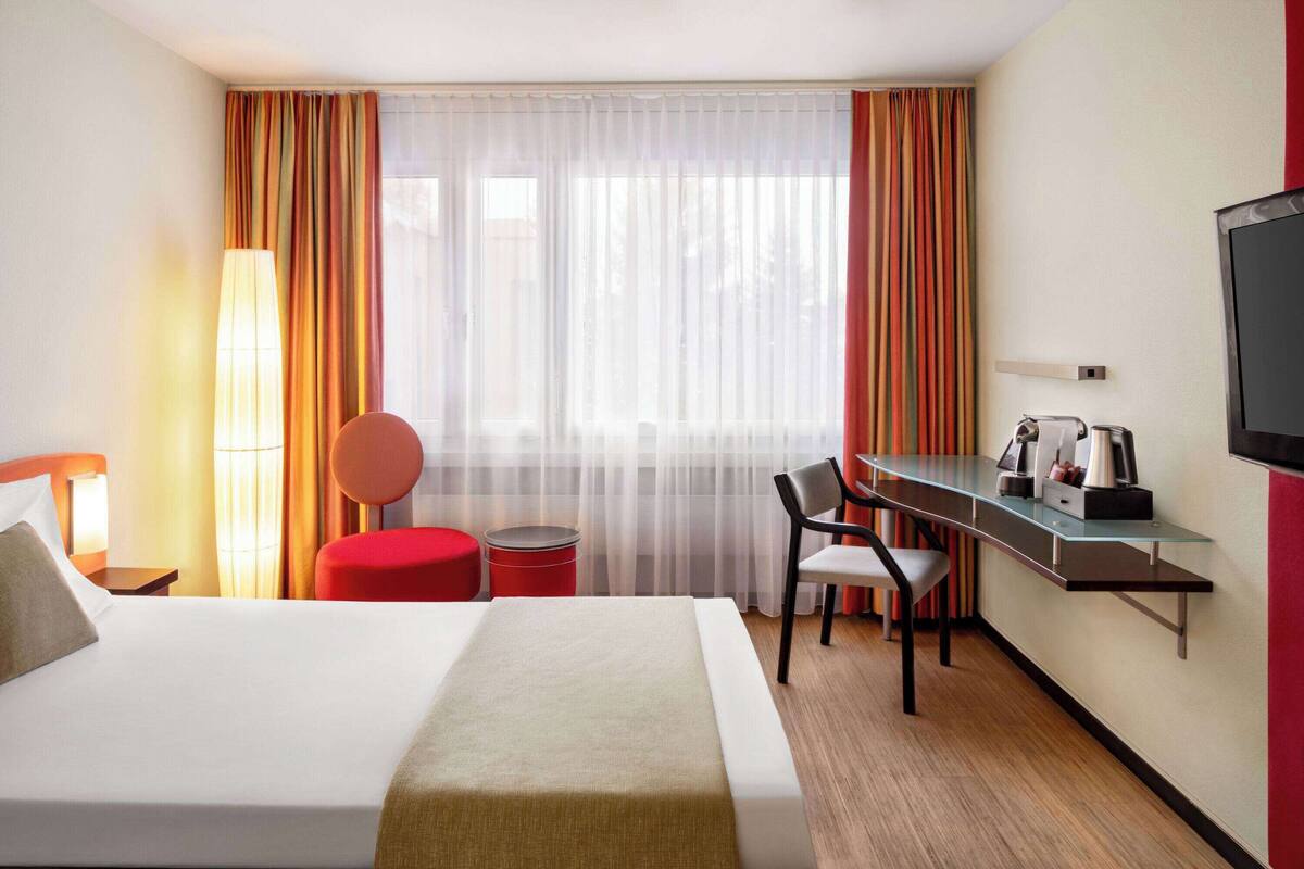 Een hotelkamer met een bed, een bureau, een stoel, een lamp en een televisie.