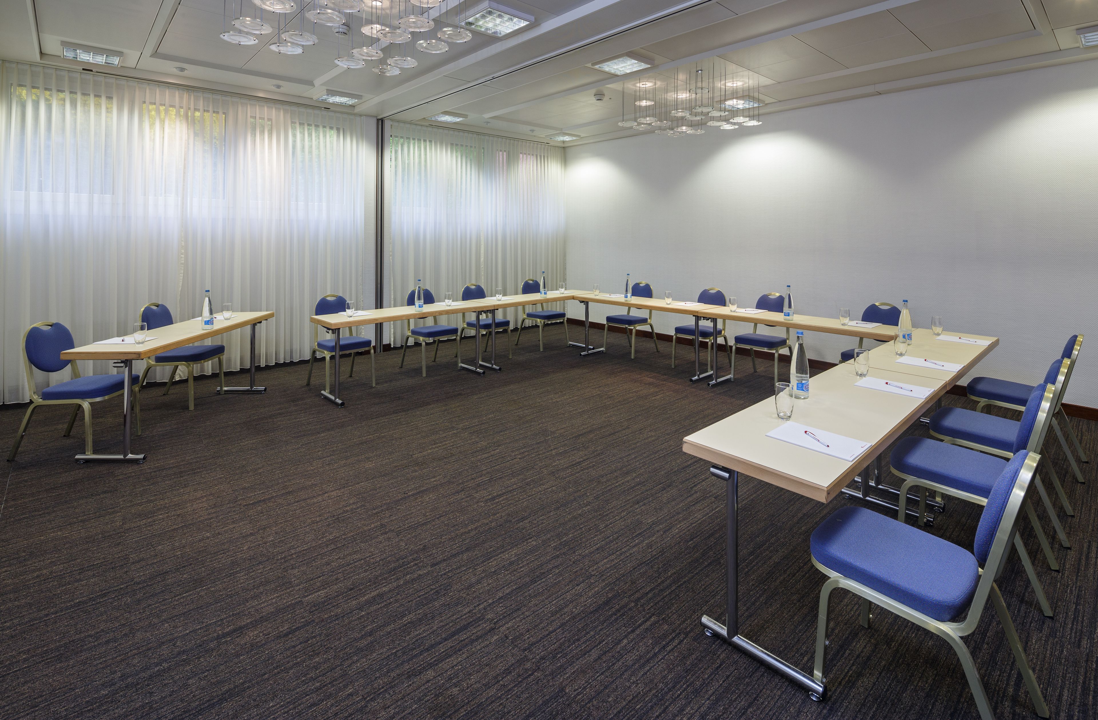 Un salón de conferencias con una larga mesa, sillas azules y piso alfombrado.