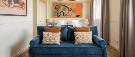 Un sofá azul con cojines estampados en una habitación con piso de madera, un ventilador de techo y un cuadro abstracto grande en la pared.