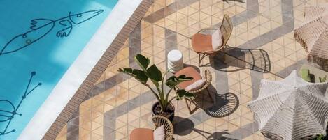 A poolside area with a geometric tile pattern, wicker furniture, and potted plants.