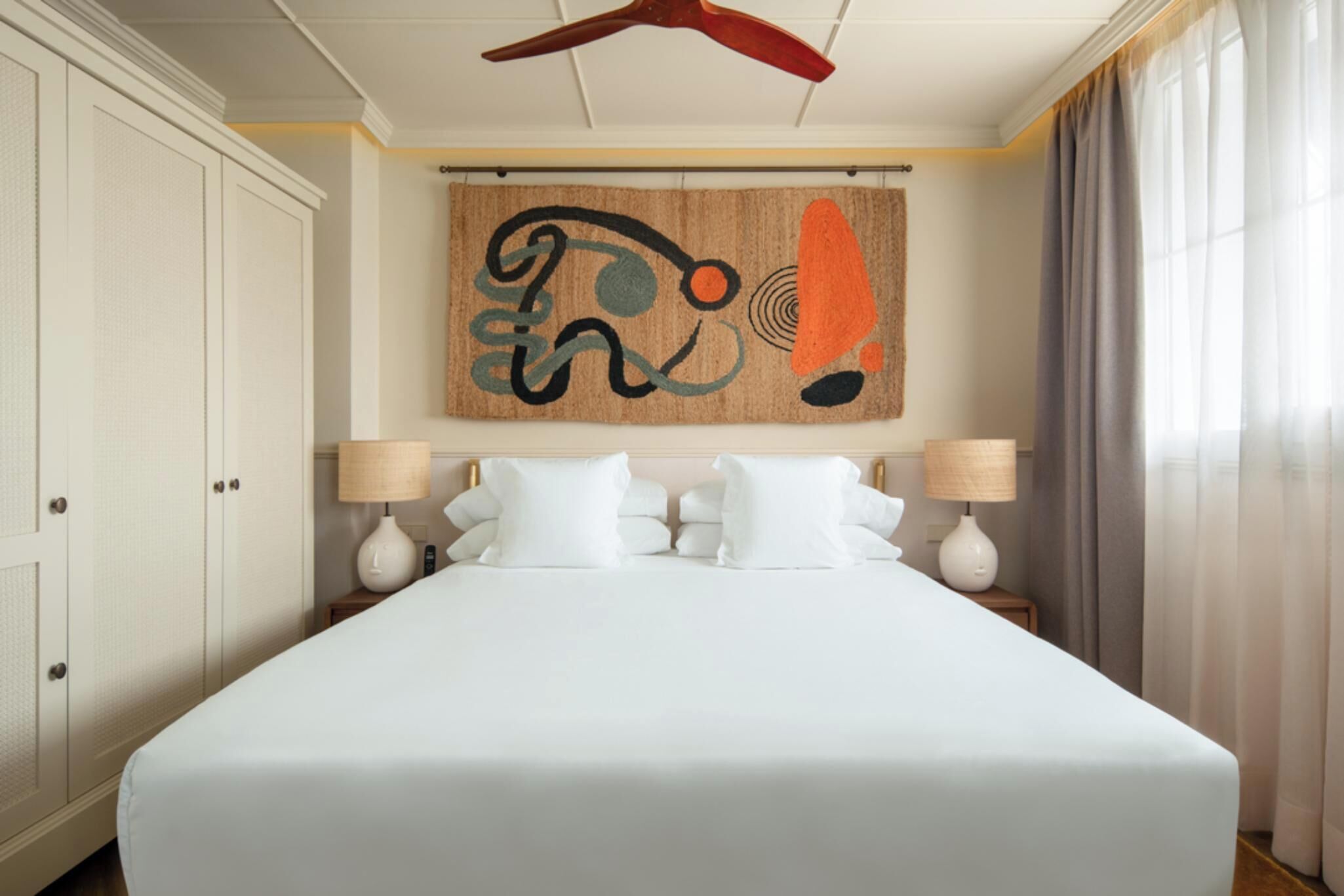A hotel room with a large bed, two bedside lamps, a ceiling fan, and a wall art piece.