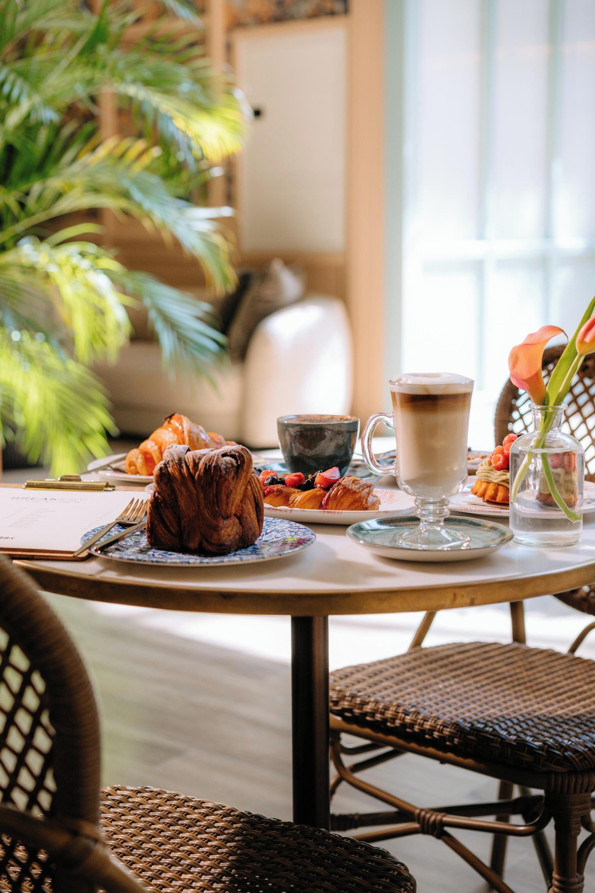 A breakfast setting with croissants, pastries, a cup of coffee, and a vase with flowers.