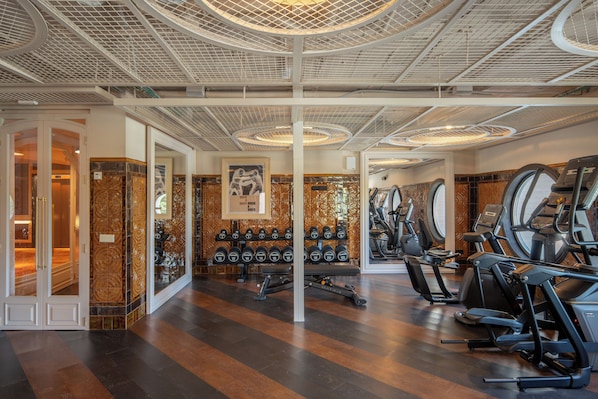 Een sportschool met fitnessapparatuur, rekken voor gewichten en een wand met een patroon.