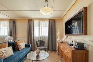 Een moderne woonkamer met een blauwe bank, een ronde salontafel, een fauteuil met een patroon, een houten kast en een flatscreen televisie die aan de muur is bevestigd.