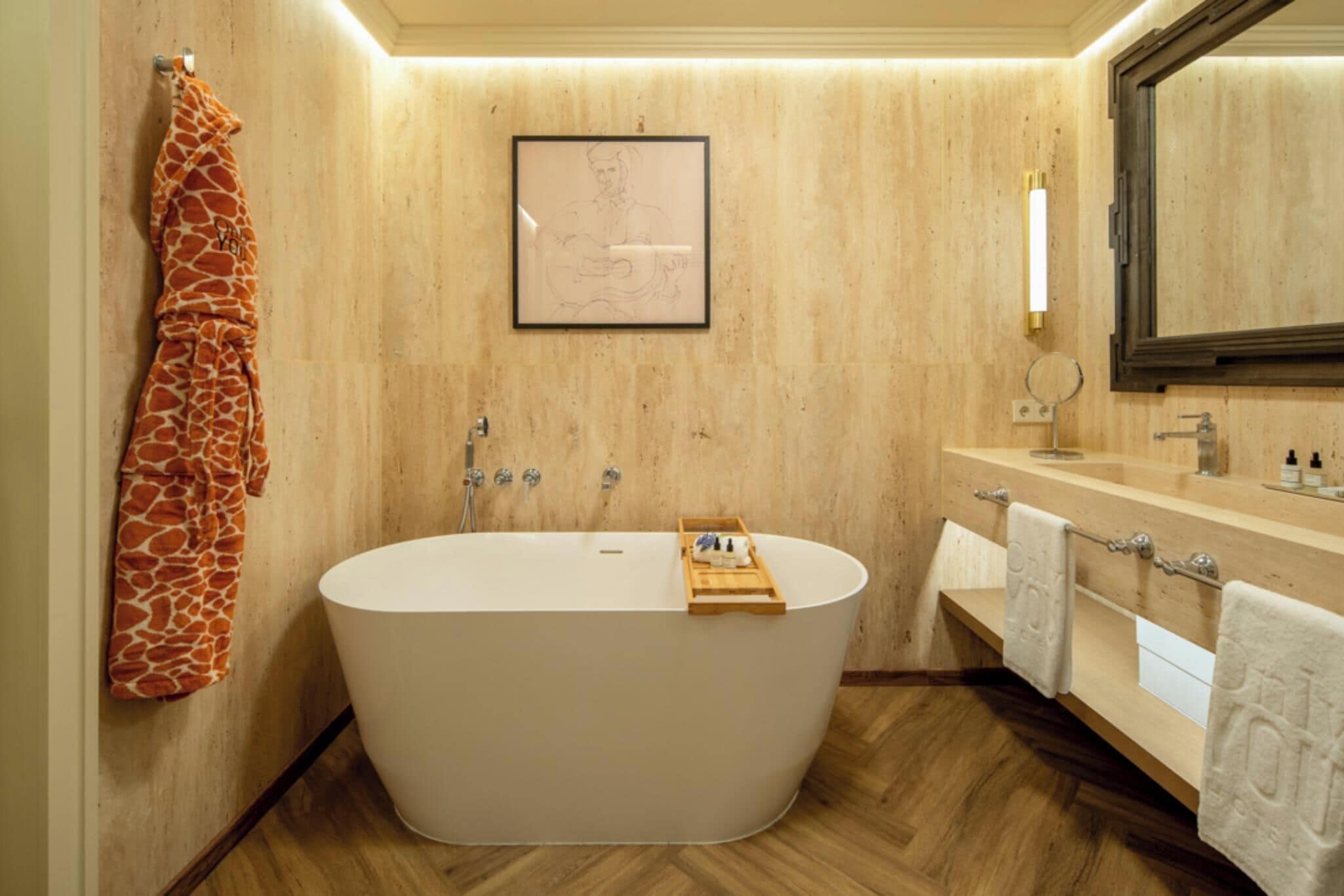 Un baño moderno con una bañera independiente, suelo de madera y un perchero con una toalla de estampado de jirafa.