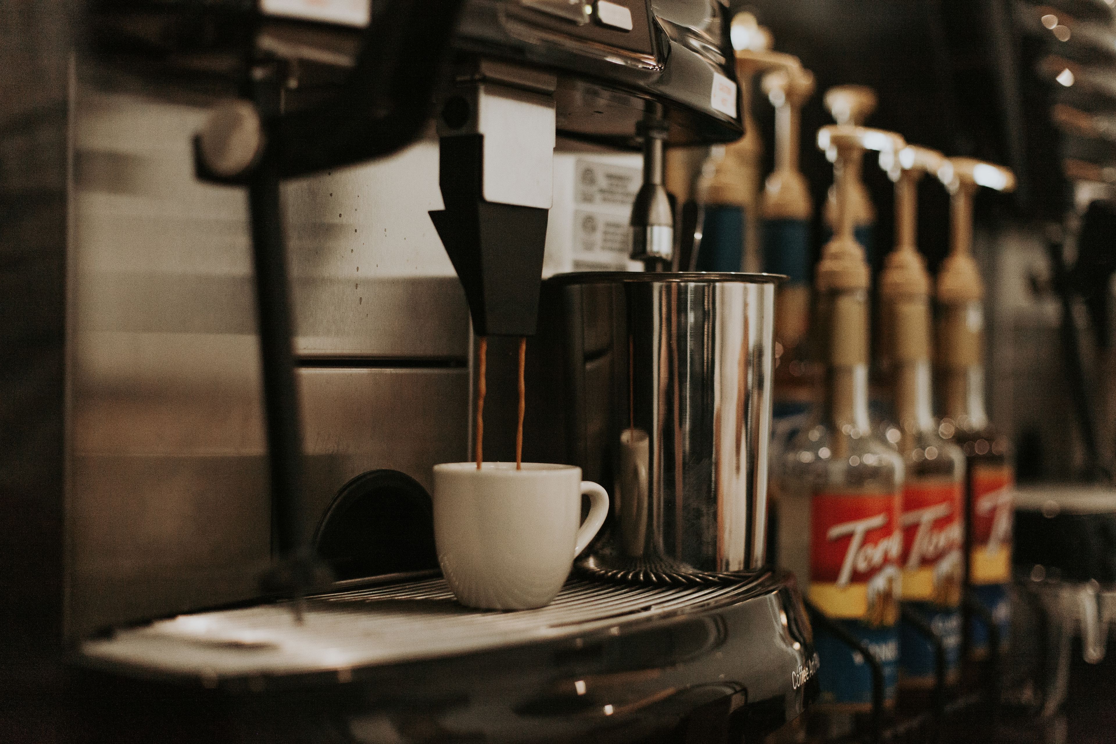A coffee machine dispensing coffee into a cup, with bottles of liquor in the background.