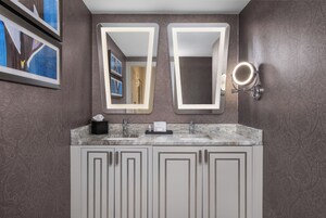 Un baño con lavamanos doble, dos espejos y tocador con armarios.