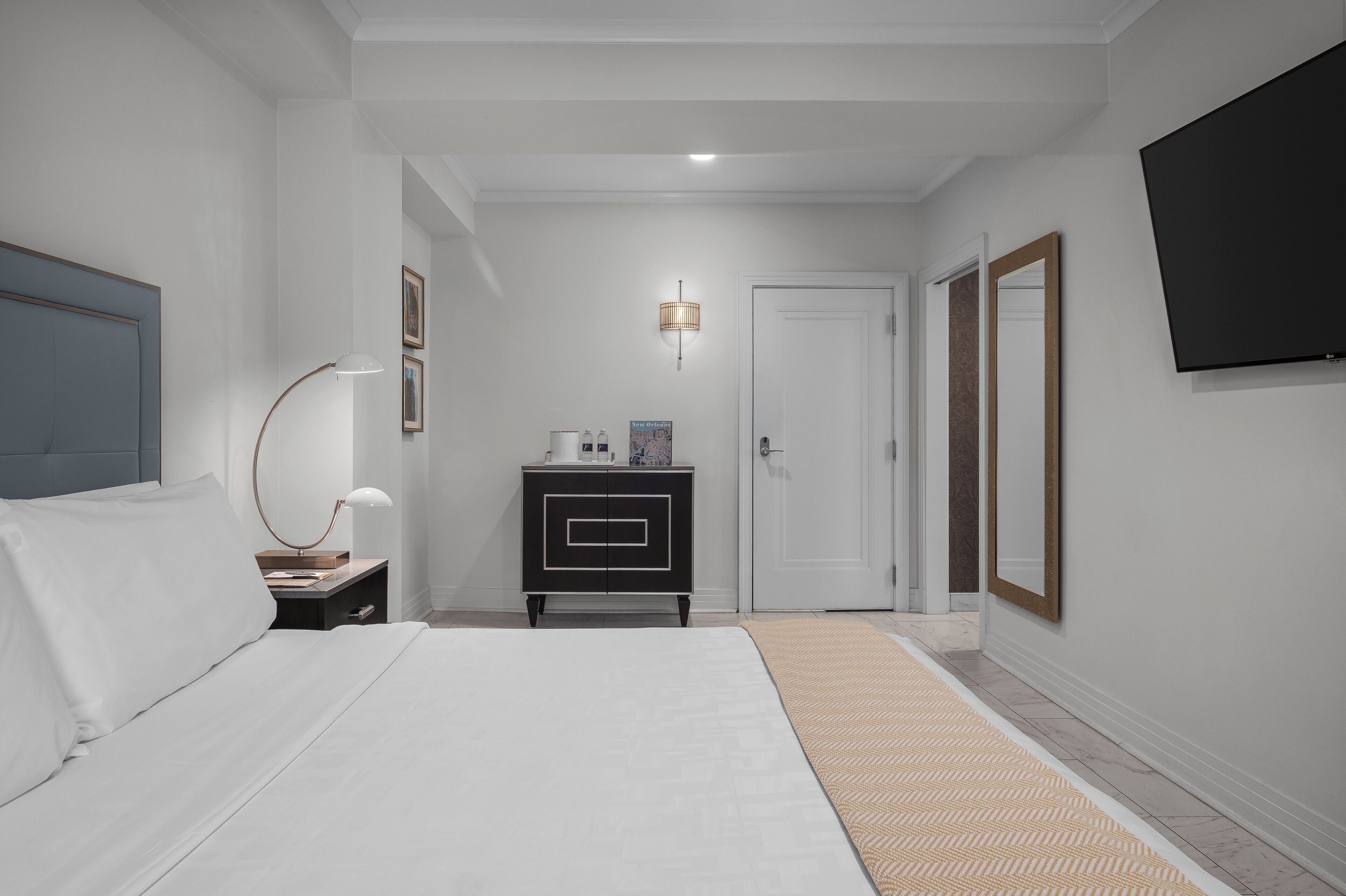 Une chambre d’hôtel équipée d’un lit, d’une table de chevet, d’une lampe, d’une commode et d’un téléviseur fixé au mur.