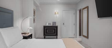 A hotel room with a bed, bedside table, lamp, dresser, and a TV mounted on the wall.