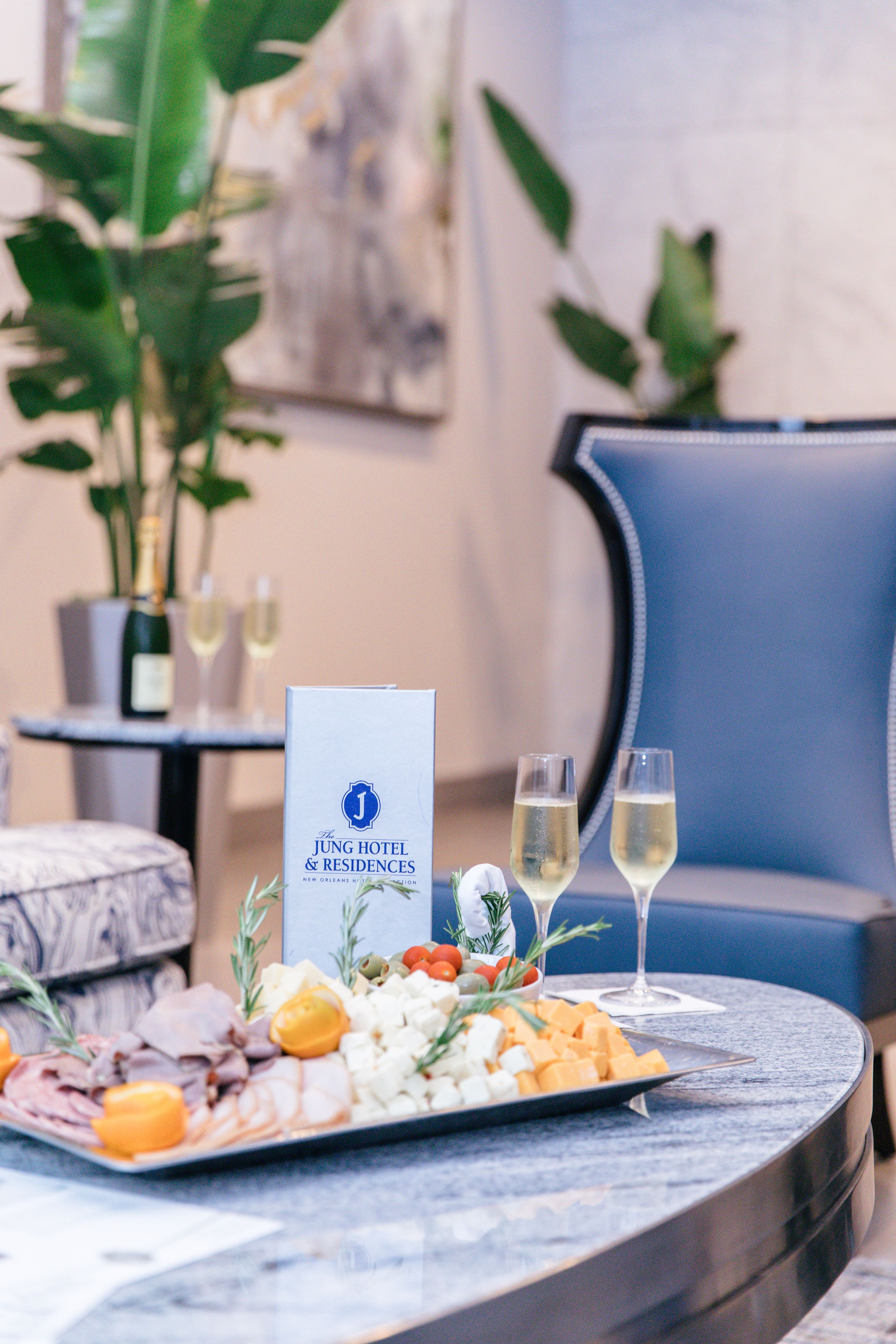 Een tafel met een vleeswarenplank, twee champagneglazen en een menukaart voor The Jung Hotel & Residences.