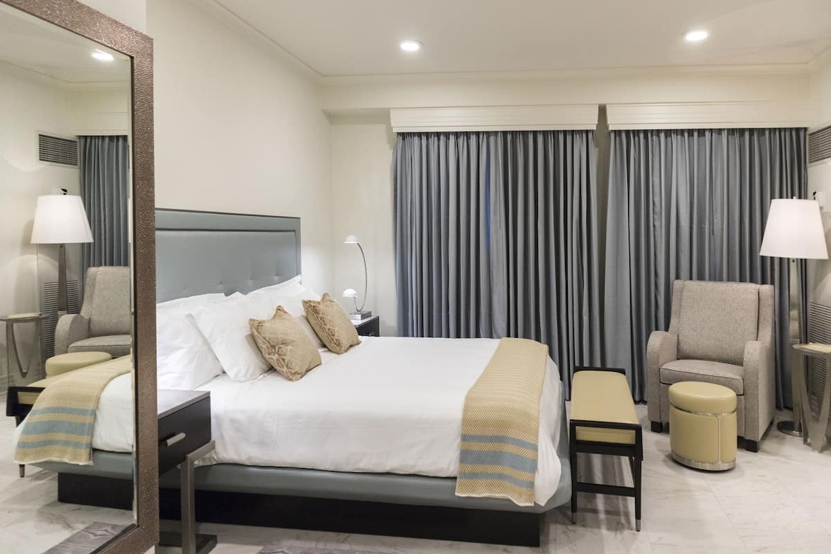 A hotel room with a bed, two chairs, a desk, a mirror, and curtains.