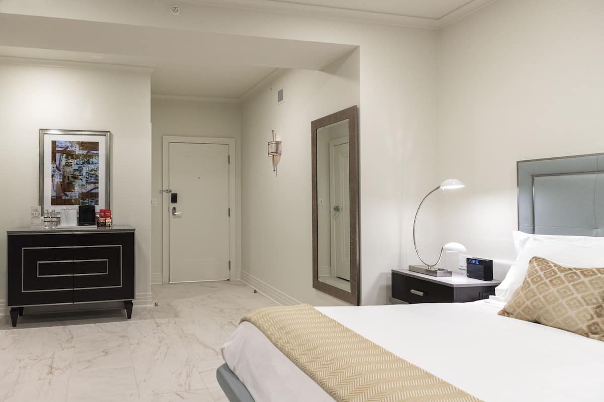 A hotel room with a bed, bedside table, lamp, and a framed picture on the wall.