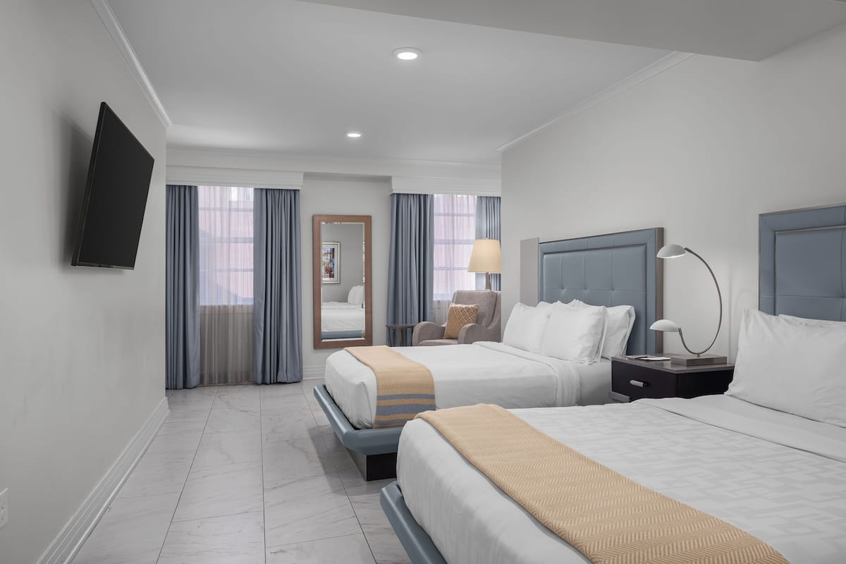 A hotel room with two beds, a flat-screen TV mounted on the wall, a nightstand with a lamp, and a chair.