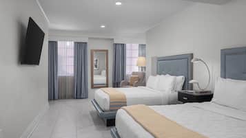 Une chambre d’hôtel avec deux lits, un téléviseur à écran plat fixé au mur, une table de chevet avec une lampe et une chaise.
