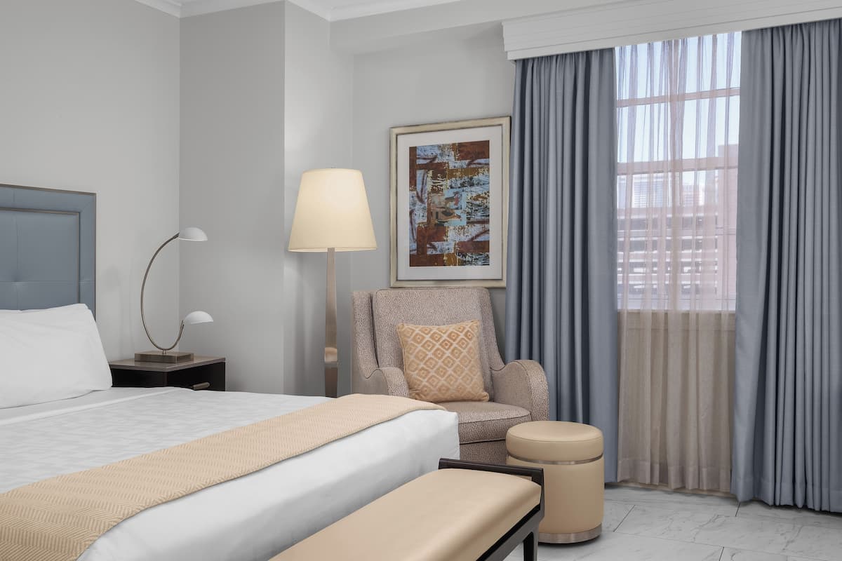 A hotel room with a bed, a chair, a lamp, a picture on the wall, and a window with curtains.