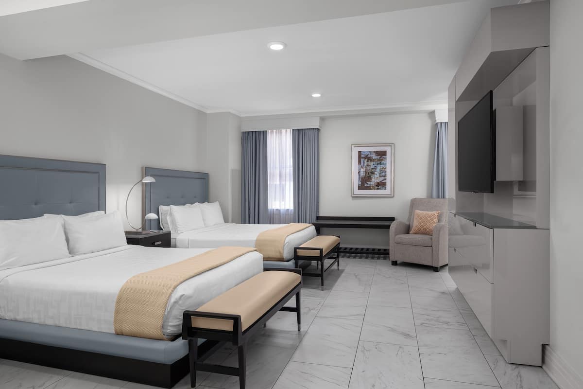 A modern hotel room with two beds, a desk, a chair, and a TV.
