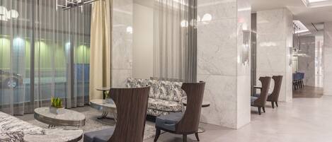 A modern lobby with marble flooring, a sofa, two armchairs, a small table, and a chandelier.