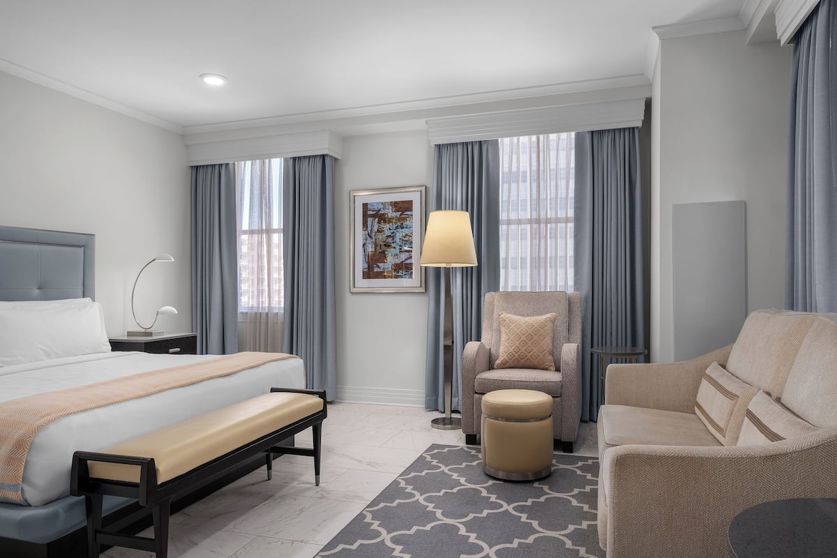 A modern hotel room with a large bed, a sofa, a chair, and a small table.