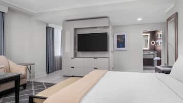 A modern hotel room with a large bed, a flat-screen TV mounted on the wall, a desk with a chair, and a small table.