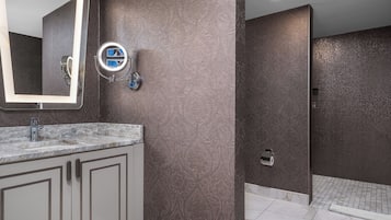 A bathroom with a marble sink, a mirror with lights, a towel rack, and a shower area.