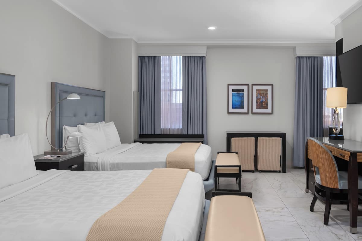 A hotel room with two beds, a desk, a chair, and a TV.